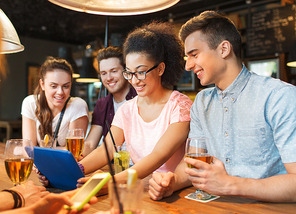 people, leisure, friendship and communication concept - group of happy smiling friends with tablet pc computer and drinks at bar or pub