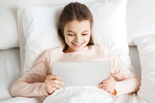people, children, rest and technology concept - happy smiling girl lying awake with tablet pc computer in bed at home
