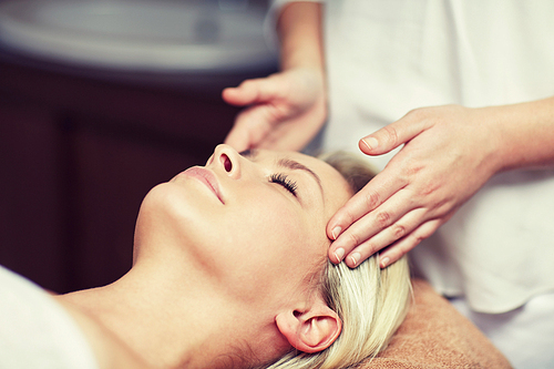 people, beauty, spa, healthy lifestyle and relaxation concept - close up of beautiful young woman lying with closed eyes and having face or head massage in spa