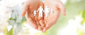 people, values and happiness concept - close up of man cupped hands showing paper family cutout over green natural background
