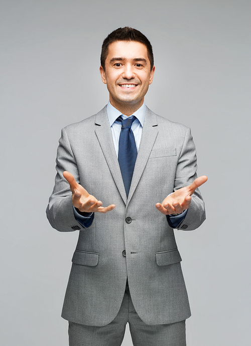 business, people, advertisement and office concept - happy businessman in suit showing or holding something imaginary on empty palms