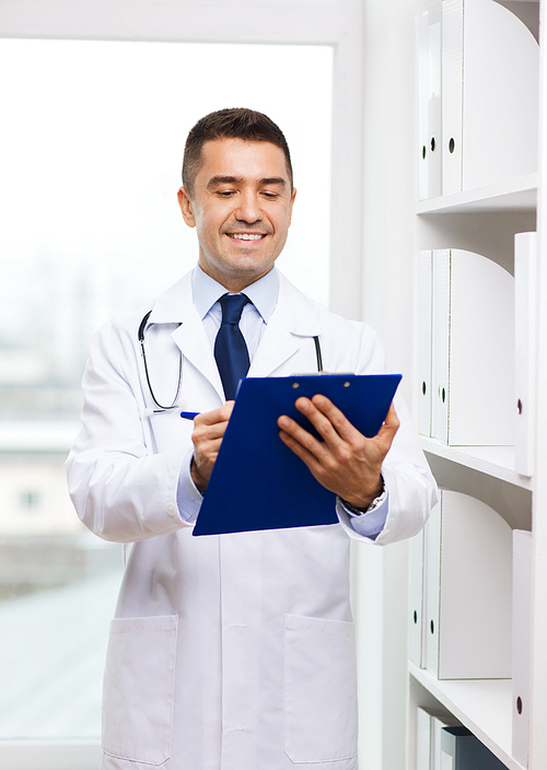 medicine, profession, technology and people concept - happy male doctor with clipboard writing diagnosis or prescription in medical office