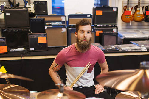 music, sale, people, musical instruments and entertainment concept - male musician at drum kit cymbals in music store