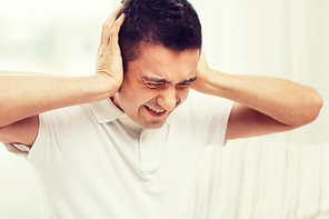 people, crisis, emotions, noise and stress concept - unhappy man closing his ears by hands at home