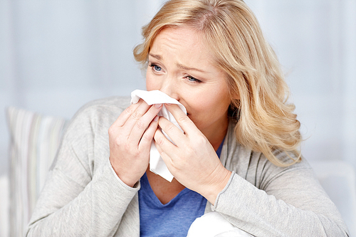 health care, flu, hygiene and people concept - ill woman blowing nose to paper napkin