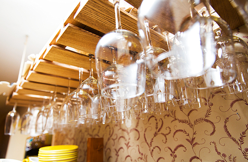 glassware, dishware and objects concept - wine glasses hanging upside down on bar holder