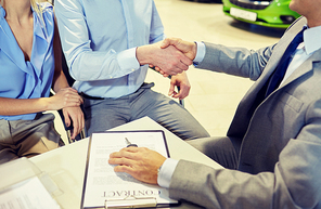 auto business, car sale, gesture and people concept - close up of customers couple with dealer shaking hands in auto show or salon