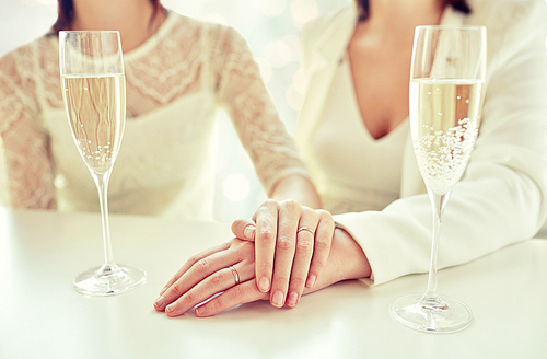 people, homosexuality, same-sex marriage, celebration and love concept - close up of happy married lesbian couple hands on top and champagne glasses over holiday lights background