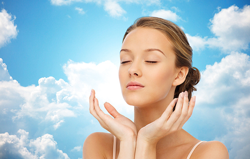 beauty, people, skincare and health concept - young woman face and hands over blue sky and clouds background