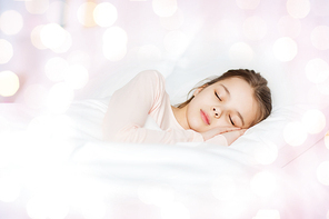 people, children, rest and comfort concept - girl sleeping in bed over lights