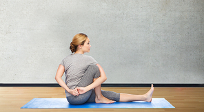 fitness, sport, people and healthy lifestyle concept - woman making yoga in twist pose on mat over gym room background