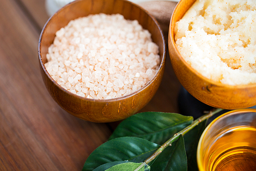 beauty, spa, body care, natural cosmetics and and wellness concept - close up of himalayan pink salt and body scrub with leaves on wooden table