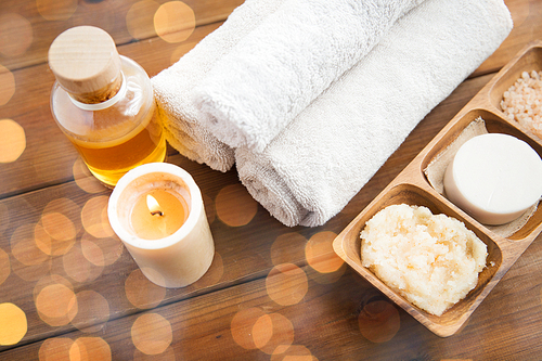 beauty, spa, body care, natural cosmetics and wellness concept - close up of soap with candle and bath towels on wooden table