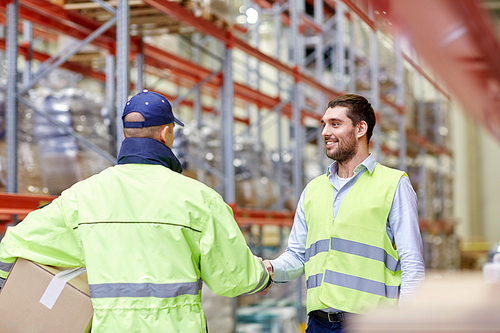 wholesale, logistic, people, agreement and export concept - manual worker and businessmen in reflective safety vests shaking hands and making deal at warehouse