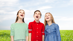 childhood, summer, emotion, friendship and people concept - happy amazed boy and girls looking up with open mouths over blue sky and grass background