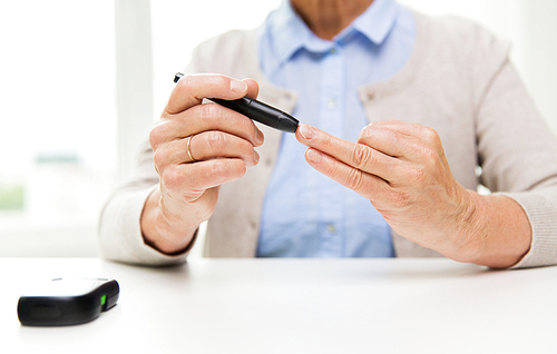 medicine, age, diabetes, health care and people concept - close up of senior woman with glucometer checking blood sugar level at home