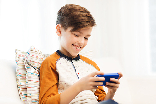 leisure, children, technology, internet communication and people concept - smiling boy with smartphone texting message or playing game at home