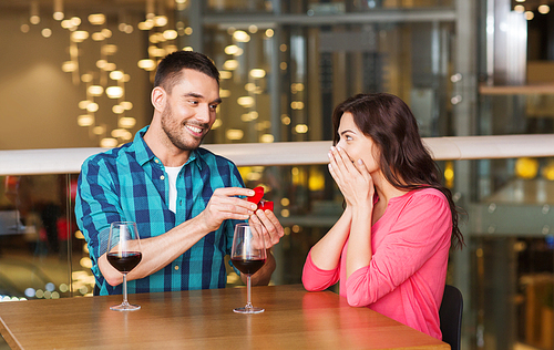 people, proposal, love, couple and holidays concept - smiling man giving diamond engagement ring to his happy girlfriend at restaurant