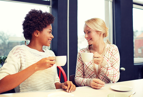 people, leisure, friendship and communication concept - happy young women meeting and drinking tea or coffee at cafe