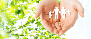 people, values and happiness concept - close up of man cupped hands showing paper family cutout over green natural background