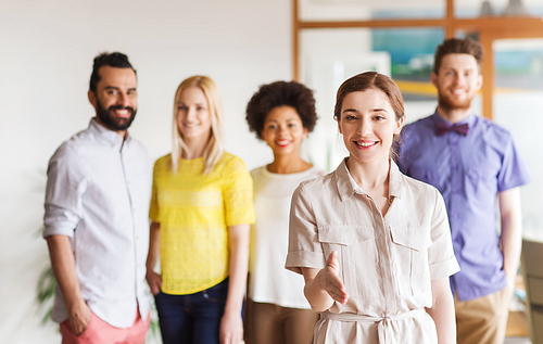 business, startup, people, gesture and teamwork concept - happy young woman greeting by handshake over creative team in office