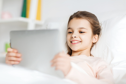 people, children, rest and technology concept - happy smiling girl lying awake with tablet pc computer in bed at home