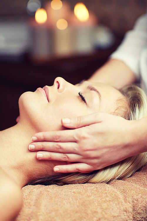 people, beauty, spa, healthy lifestyle and relaxation concept - close up of beautiful young woman lying with closed eyes and having face or head massage in spa