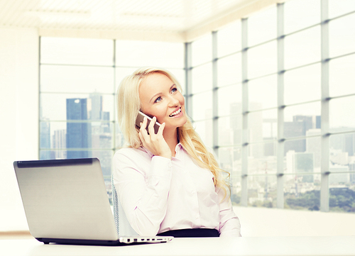 business, communication, people and technology concept - smiling businesswoman or secretary with laptop computer calling on smartphone over office room with city view window background