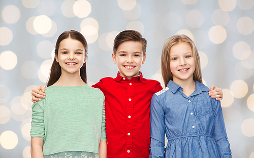 childhood, fashion, friendship and people concept - happy smiling boy and girls hugging over holidays lights background