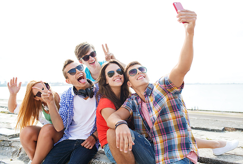 friendship, leisure, summer, technology and people concept - group of happy friends with smartphone taking selfie outdoors