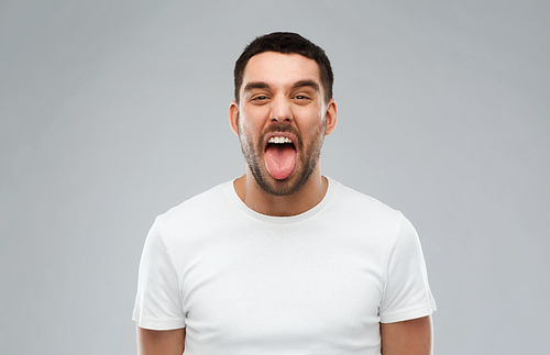 expression, rudeness and people concept - man showing his tongue over gray background