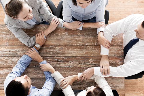 business, people, cooperation and team work concept - close up of creative team sitting at table and holding hands in office