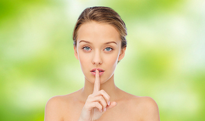 people, silence, secret, gesture and beauty concept - beautiful young woman holding finger on lips over green natural background