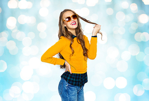 people, style and fashion concept - happy young woman or teen girl in casual clothes and sunglasses over blue holidays lights background