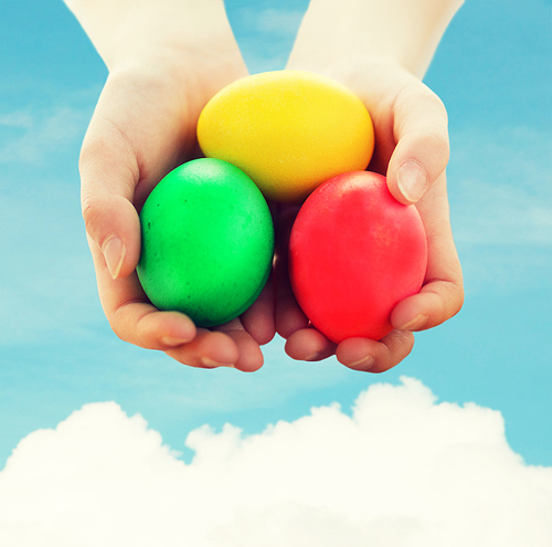 easter, holiday and child concept - close up of kid hands holding colored eggs over blue sky and white cloud background