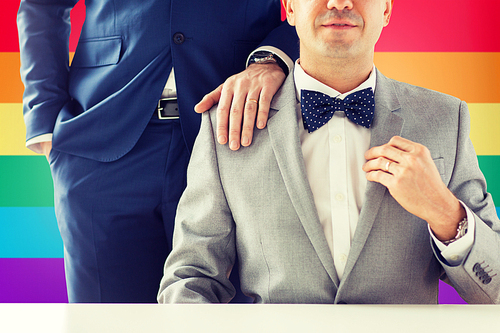 people, celebration, homosexuality, same-sex marriage and love concept - close up of male gay couple with wedding rings on putting hand on shoulder over  flag background