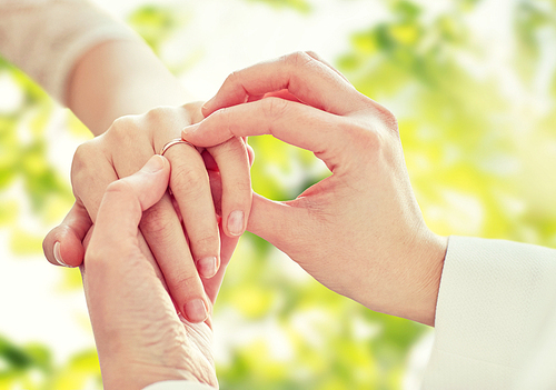 people, homosexuality, same-sex marriage, summer and love concept - close up of happy lesbian couple hands putting on wedding ring over green tree leavers background