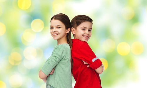 childhood, fashion and people concept - happy smiling boy and girl standing back to back over green lights background