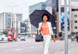 business and people concept - young smiling african american businesswoman with umbrella and handbag walking down city street