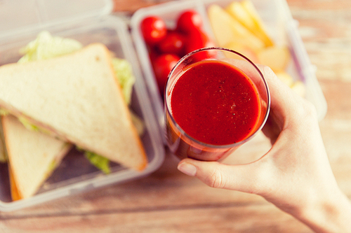 healthy eating, dieting and people concept - close up of woman hand holding fresh tomato juice glass over food in plastic container at home