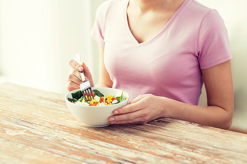 healthy eating, dieting and people concept - close up of young woman eating vegetable salad at home