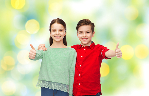 childhood, fashion, gesture and people concept - happy smiling boy and girl hugging and showing thumbs up over green lights background