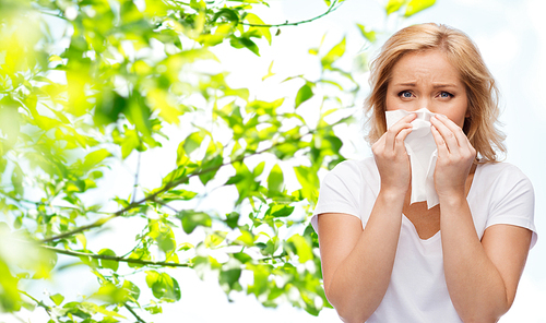 people, healthcare, rhinitis, cold and allergy concept - unhappy woman with paper napkin blowing nose over natural background