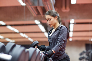 fitness, sport, exercising, weightlifting and people concept - young woman choosing dumbbells in gym