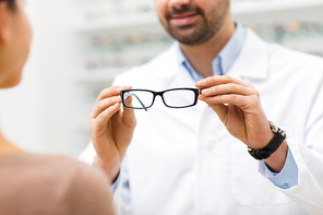 health care, people, eyesight and vision concept - close up of optician showing glasses to woman at optics store