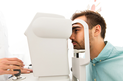 health care, medicine, people, eyesight and technology concept - close up of optometrist with autorefractor checking patient vision at eye clinic or optics store