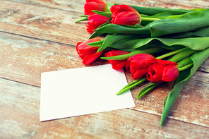 advertisement, valentines day, greeting and holidays concept - close up of red tulips and blank paper or letter on wooden background