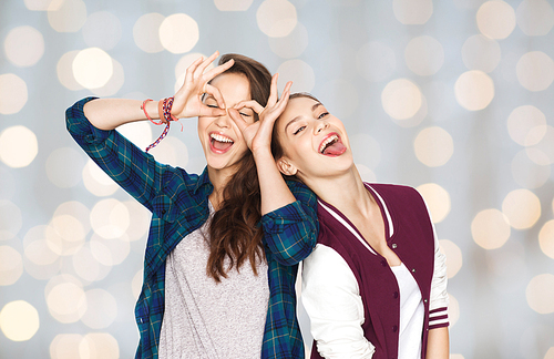 people, friends, teens and friendship concept - happy smiling pretty teenage girls having fun and making faces over holidays lights background