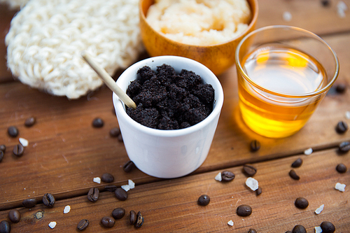 beauty, spa, body care, bath and natural cosmetics concept - close up of coffee scrub in cup and honey on wooden table