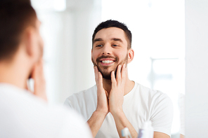 beauty, hygiene and people concept - smiling young man looking to mirror at home bathroom